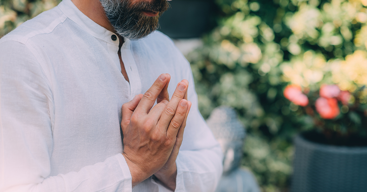 Gratefulness meditation. Peaceful man sitting in a lotus pose and meditating, keeping hands together in a prayer position.